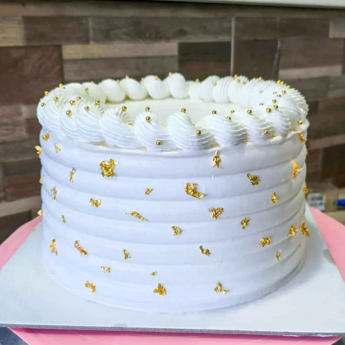 A white buttercream cake with gold flecks and a piped top border