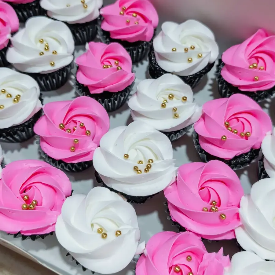 Chocolate cupcakes piped with pink and white buttercream roses and gold pearls