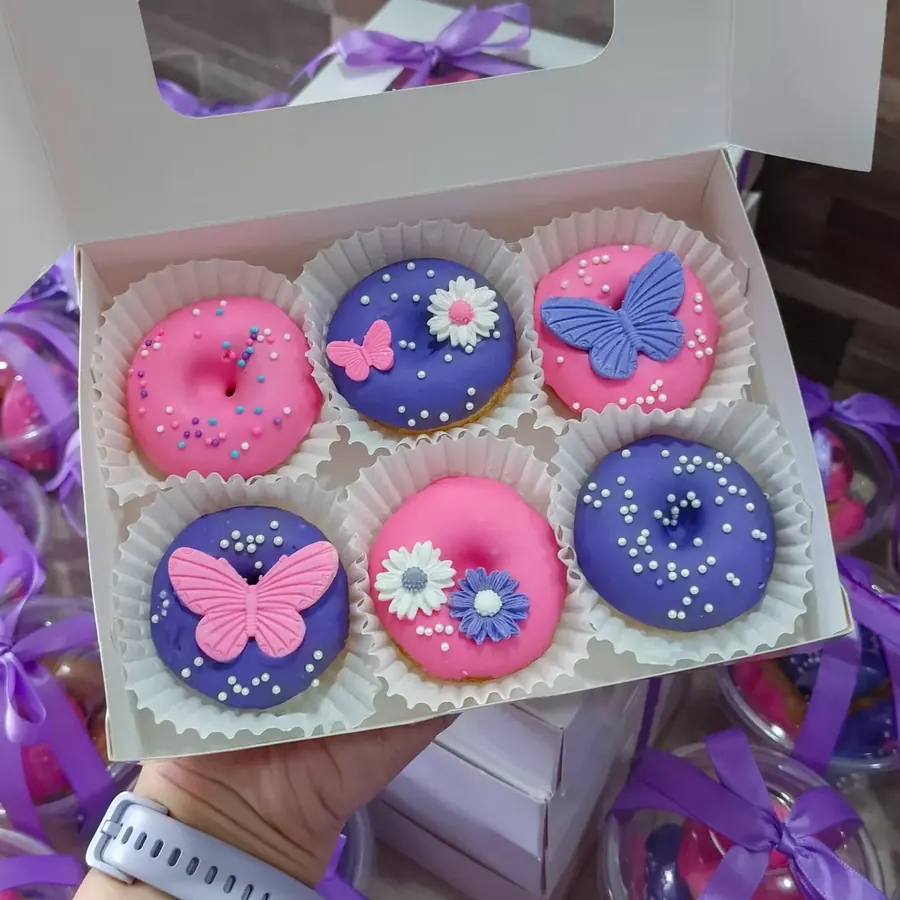 Pink and purple mini donuts with fondant butterflies and daisies in a white box
