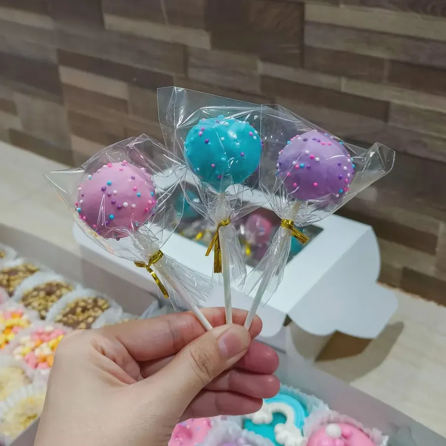 Pastel cake pops with sprinkles held up on sticks